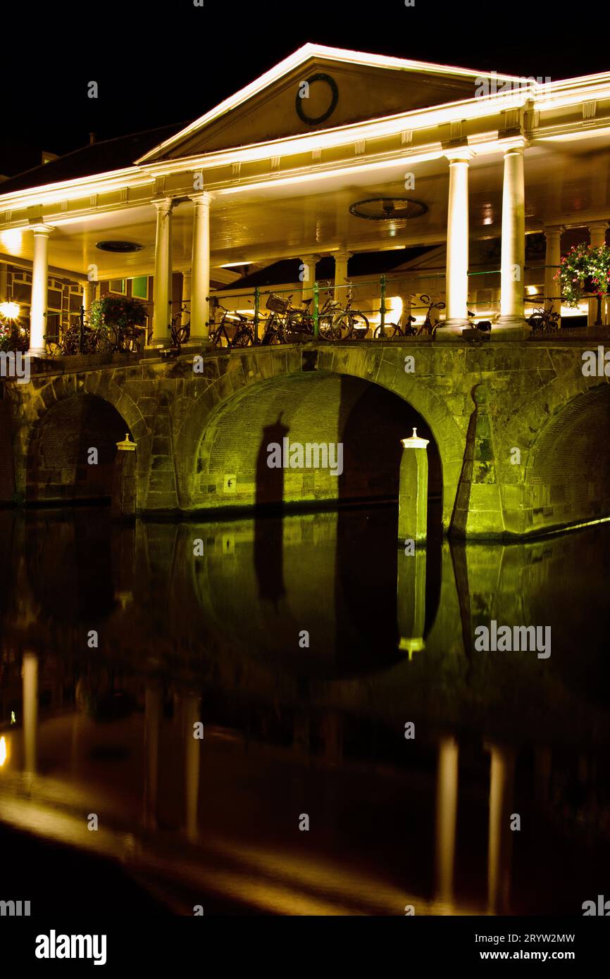 Un pont de pierre illuminé la nuit, avec un grand bâtiment en arrière-plan : Leiden Banque D'Images