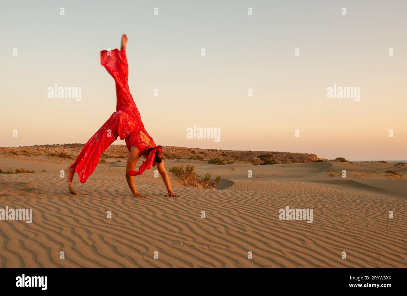 Jeune femme attirante vêtue d'exercices rouges sur les dunes de sable dans le désert contre le ciel bleu Banque D'Images