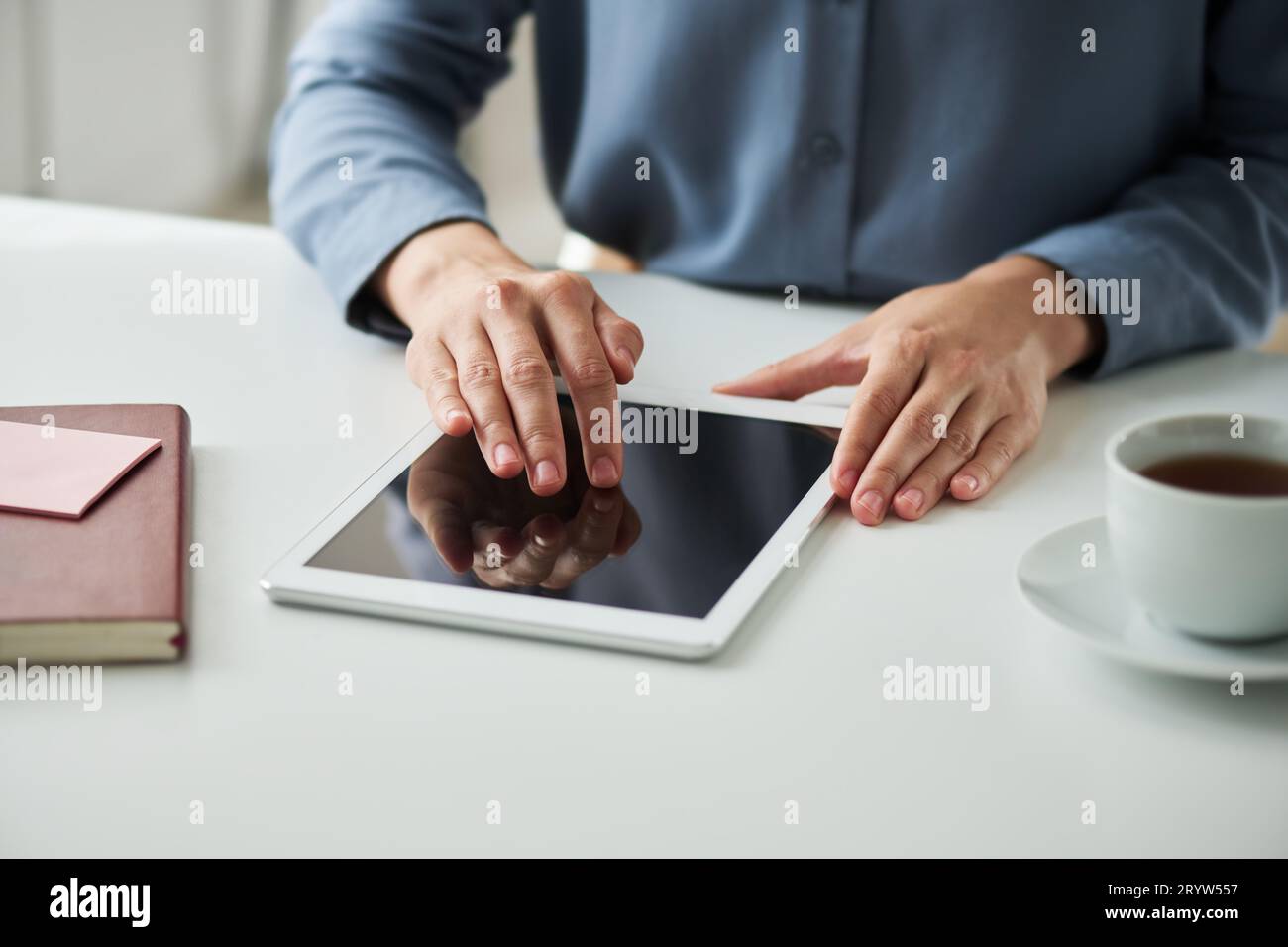 Mains de la jeune femme assise par le bureau et faire défiler les messages en ligne, le texte d'article ou d'autres choses sur l'écran de la tablette tout en étant assis par le bureau Banque D'Images