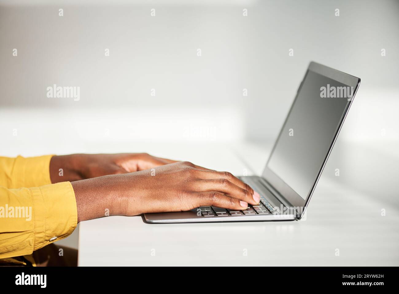 Vue latérale des mains de jeune employé masculin tapant sur le clavier d'ordinateur portable tout en étant assis par le bureau devant la caméra et travaillant sur le nouveau projet Banque D'Images