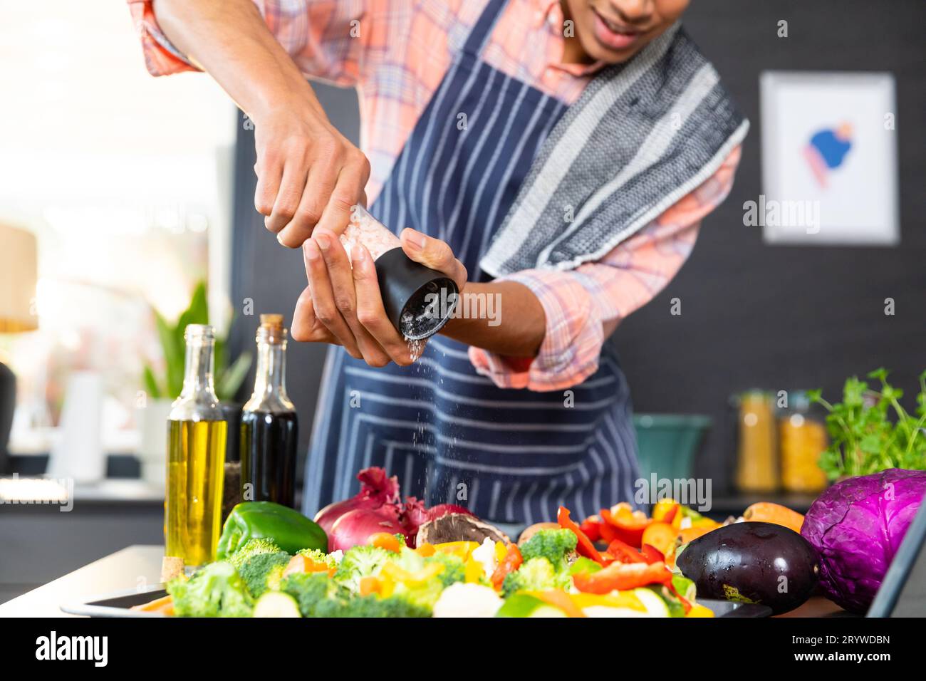 Section médiane de l'homme biracial portant un tablier cuisinant le dîner, assaisonnant les légumes dans la cuisine Banque D'Images