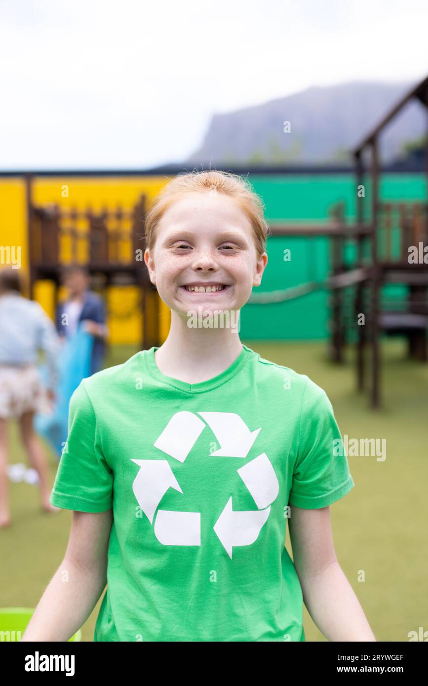 Portrait vertical d'une fille caucasienne souriante portant un t-shirt de recyclage dans la cour d'école, avec espace de copie Banque D'Images