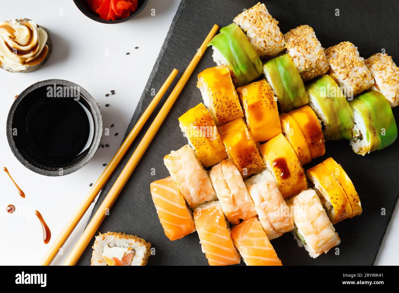 Mettre rouleau avec saumon, avocat, crevettes et anguille sur une planche de pierre avec wasabi et sauce soja sur un fond clair, vue de dessus. Banque D'Images