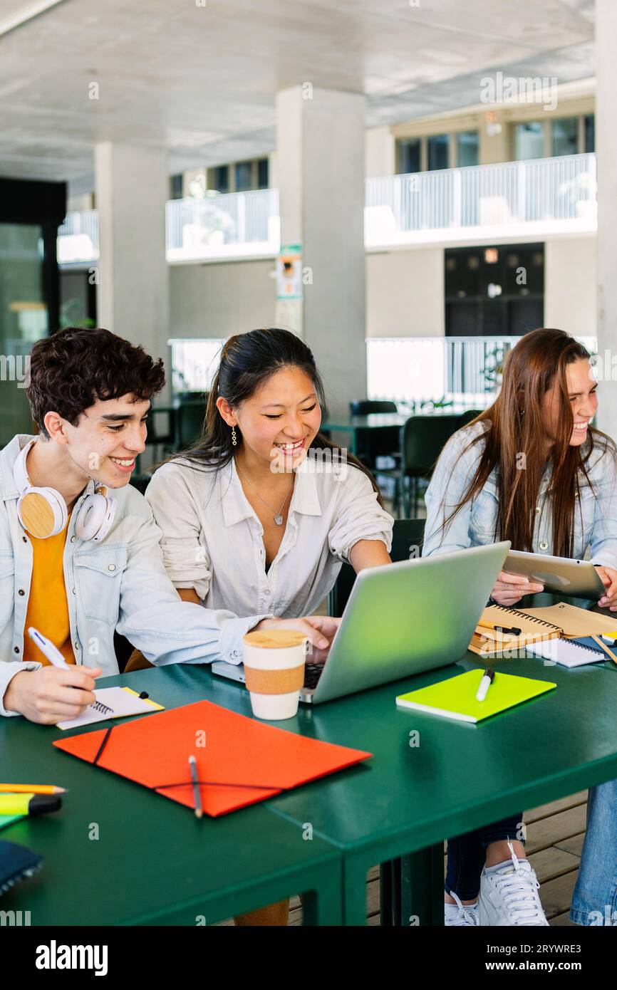 Heureux jeune groupe d'étudiants multiraciaux travaillant ensemble sur ordinateur portable à l'université Banque D'Images