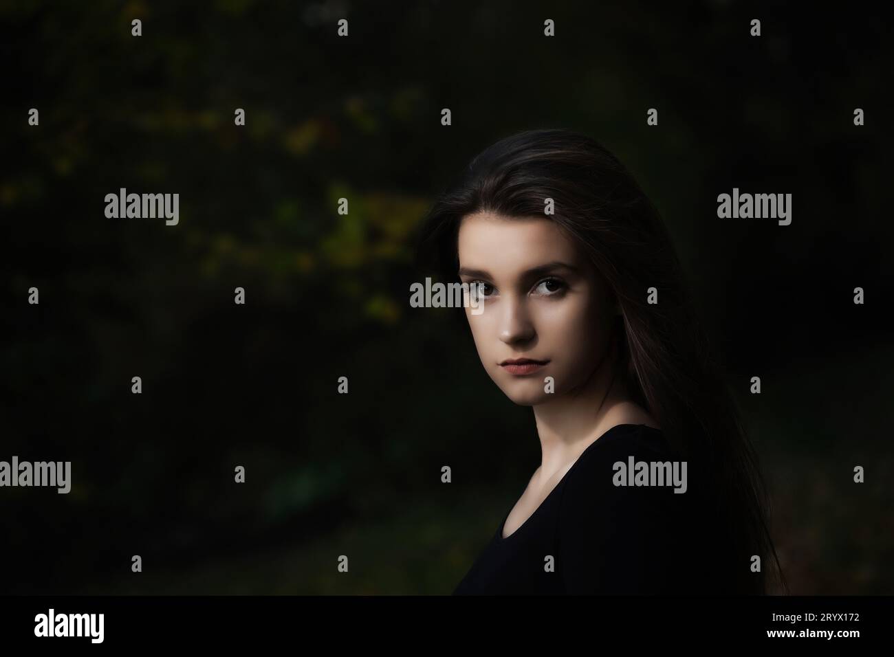 Portrait de fille aux cheveux longs cool posant à l'extérieur sur fond sombre. Horizontalement. Banque D'Images