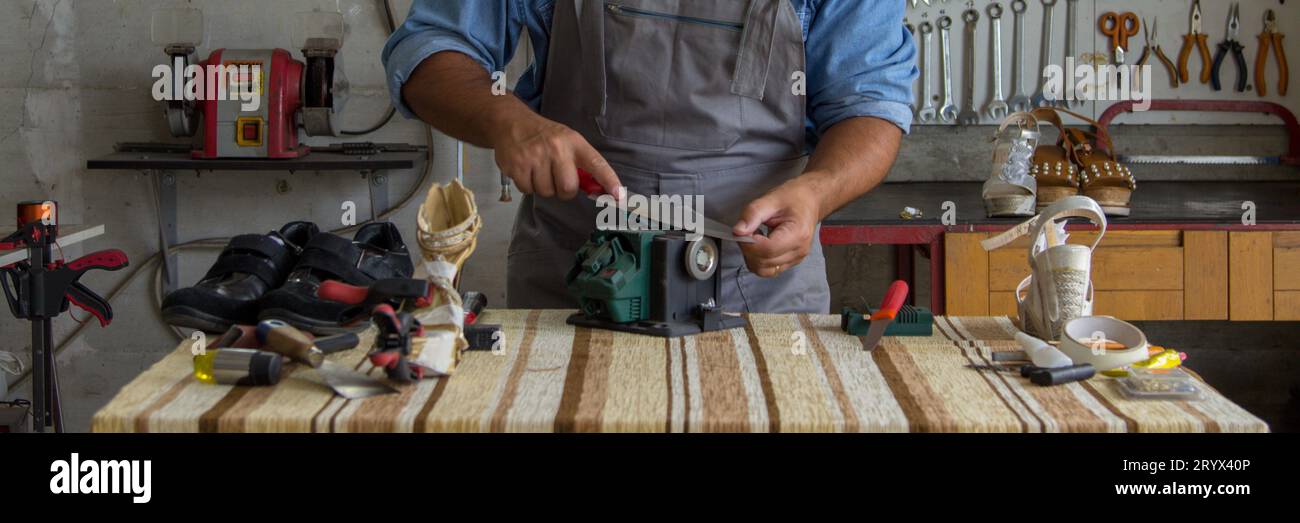 Image d'un cordonnier affûtant un couteau de cuisine avec une meule d'affûtage. Bannière horizontale Banque D'Images