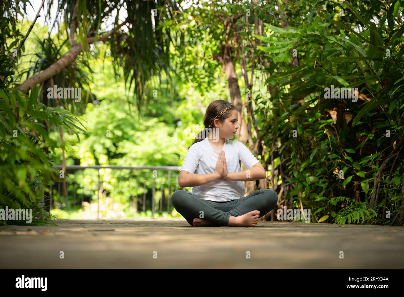 Petite fille dans le jardin il y a des allées en bois et un tunnel d'arbres verts frais, avec des activités de yoga pour la santé Banque D'Images