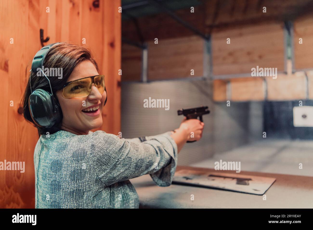 Une femme s'entraîne à tirer un pistolet dans un stand de tir tout en portant un casque de protection Banque D'Images