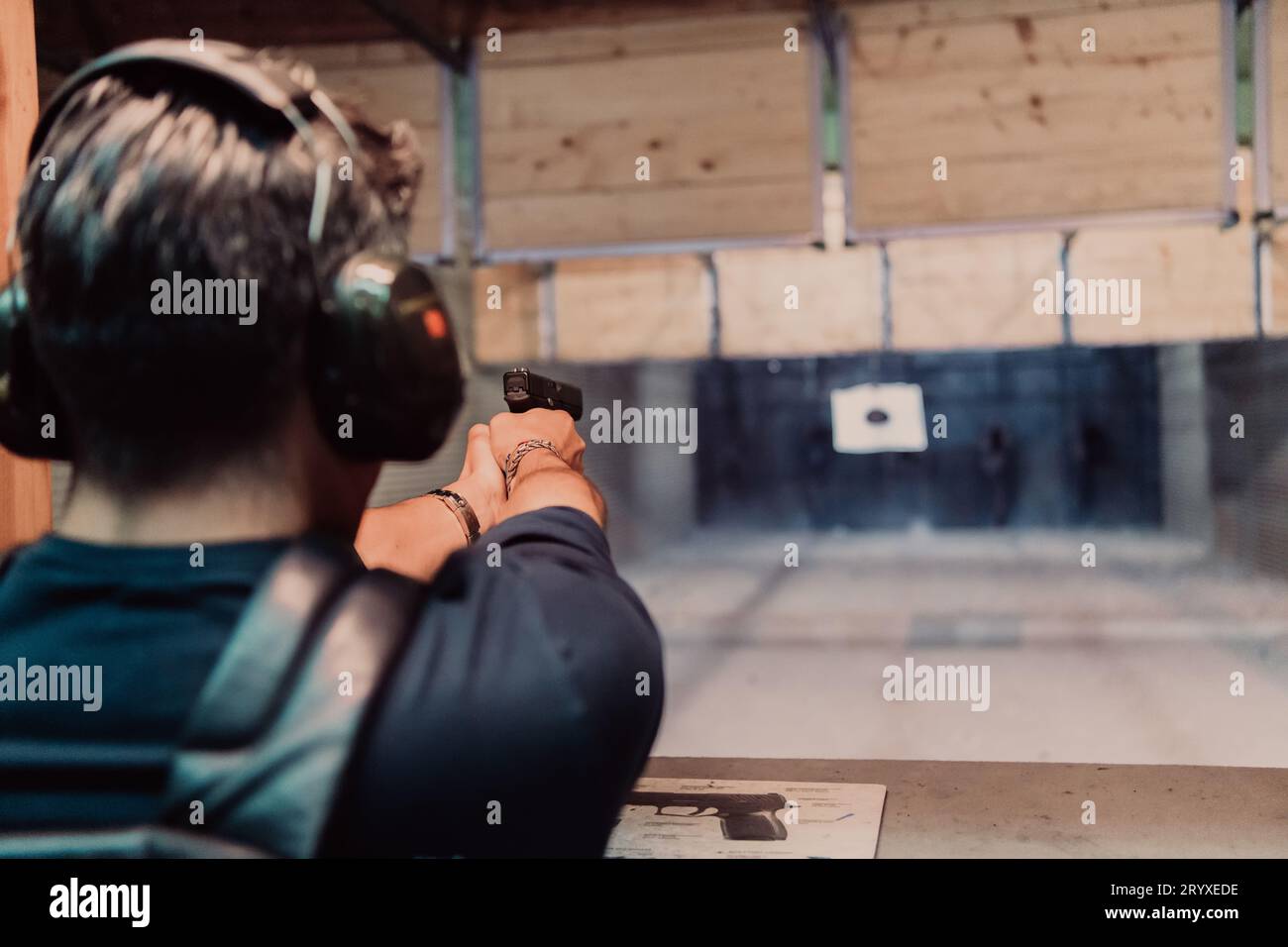 Un homme pratique le tir d'un pistolet dans une gamme de tir tout en portant des écouteurs de protection Banque D'Images