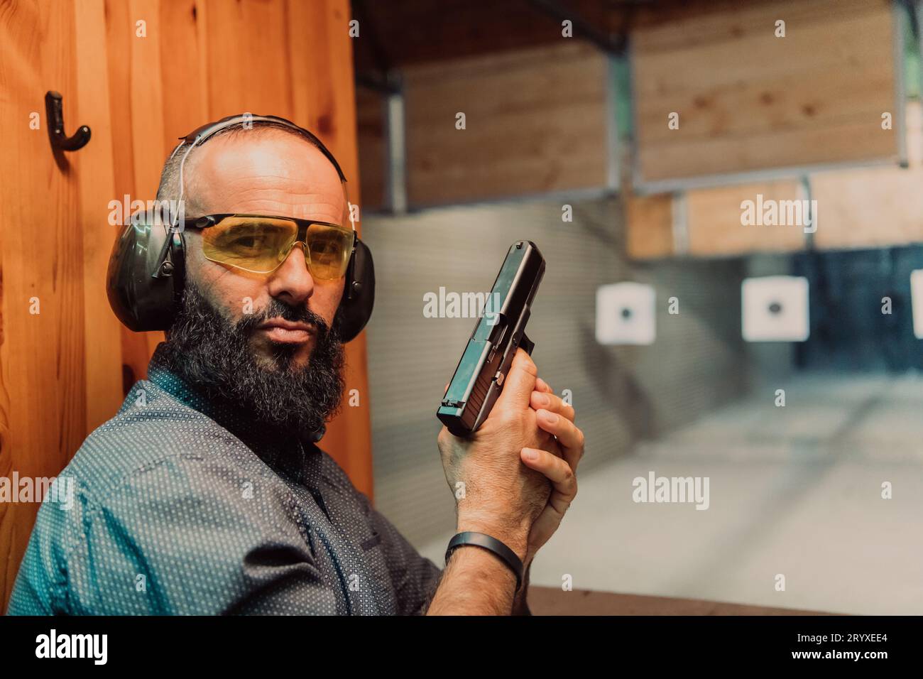 Un homme pratique le tir d'un pistolet dans une gamme de tir tout en portant des écouteurs de protection Banque D'Images