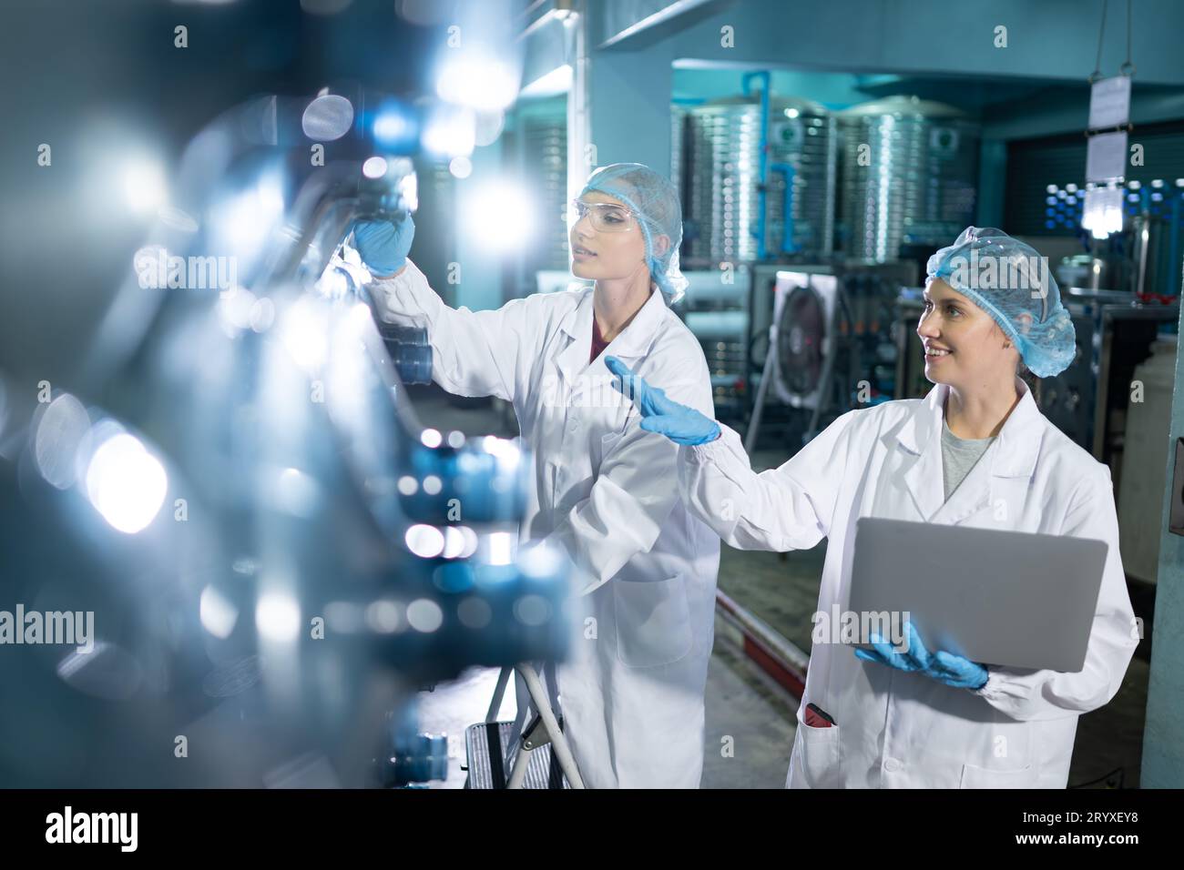 Portrait d'un scientifique dans l'usine d'eau potable utilisant une échelle, regardant les réservoirs d'eau au-dessus et examinant avec un coll. Banque D'Images