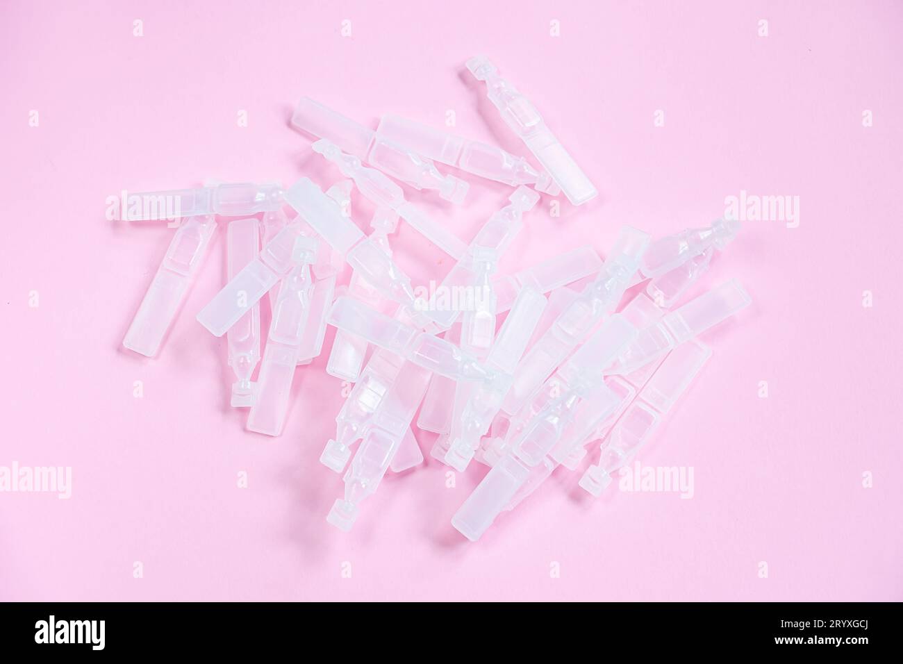 Gouttes ophtalmiques médicales dans des pipettes en plastique sur fond rose. Pile d'ampoules en plastique vides pour les gouttes. Flacons en plastique de solution saline Banque D'Images