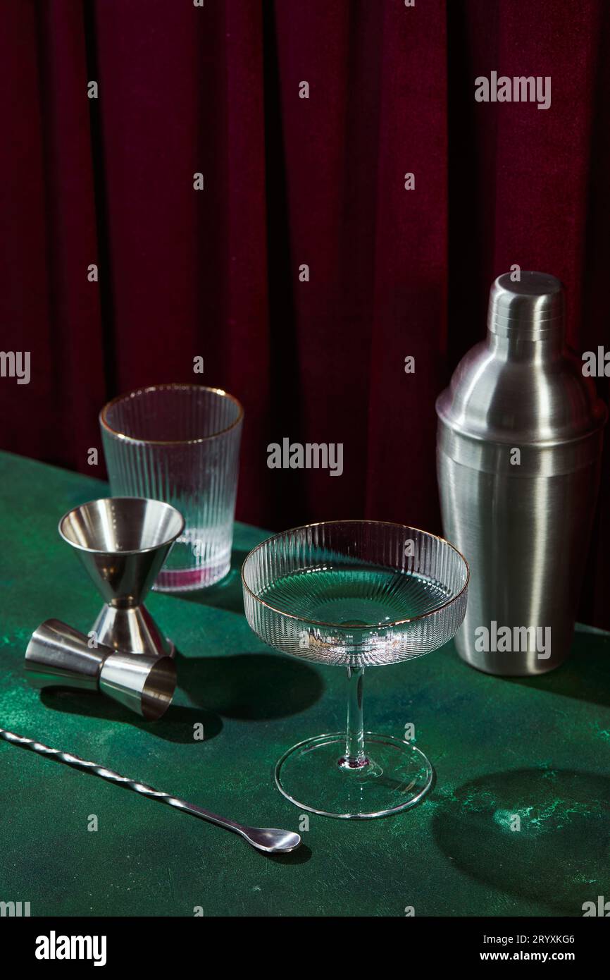 Verre à champagne, shaker, cuillère à cocktail et jigger sur la table vert foncé Banque D'Images