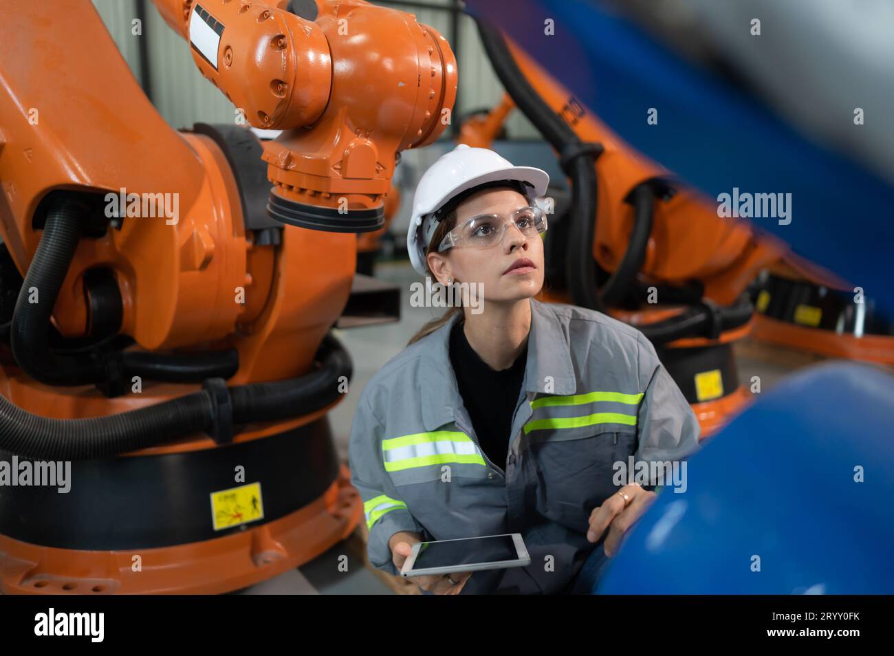 Une ingénieure installe un programme sur un bras robotique dans un entrepôt de robots. Et tester l'opération avant d'envoyer la machine t Banque D'Images