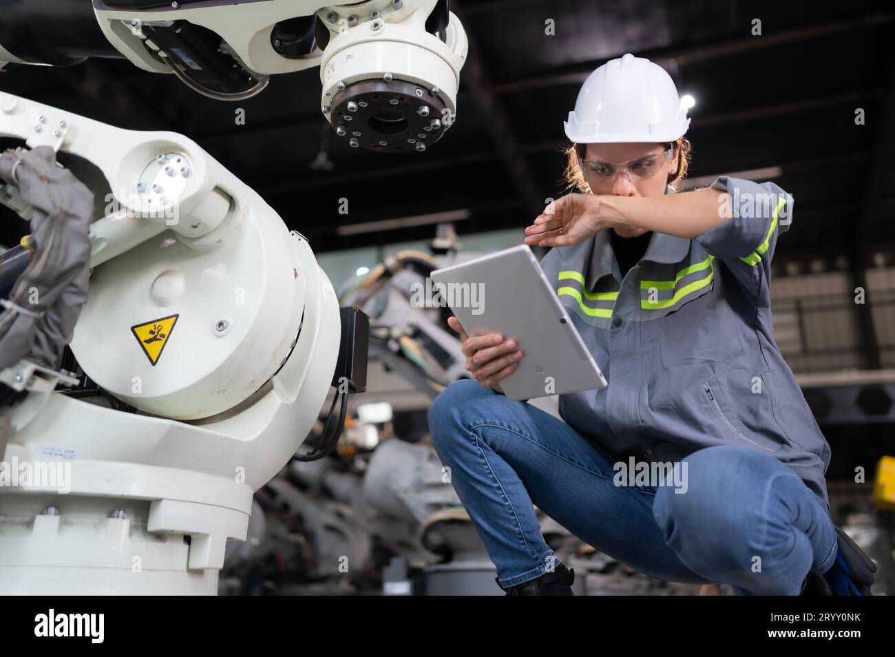 Une ingénieure installe un programme sur un bras robotique dans un entrepôt de robots. Et tester l'opération avant d'envoyer la machine t Banque D'Images