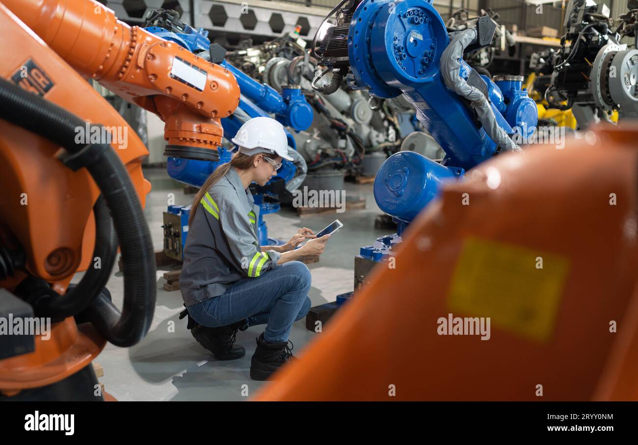 Une ingénieure installe un programme sur un bras robotique dans un entrepôt de robots. Et tester l'opération avant d'envoyer la machine t Banque D'Images