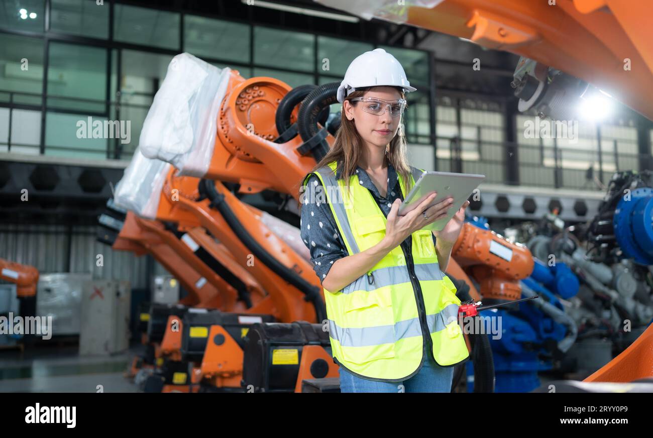 Une ingénieure installe un programme sur un bras robotique dans un entrepôt de robots. Et tester l'opération avant d'envoyer la machine t Banque D'Images