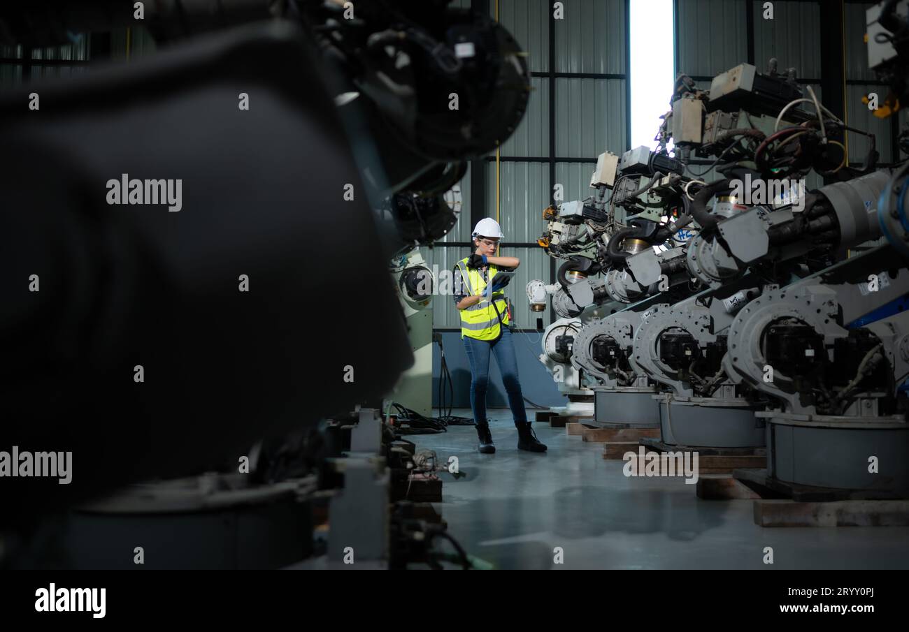 Une ingénieure installe un programme sur un bras robotique dans un entrepôt de robots. Et tester l'opération avant d'envoyer la machine t Banque D'Images