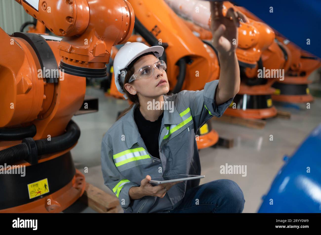 Une ingénieure installe un programme sur un bras robotique dans un entrepôt de robots. Et tester l'opération avant d'envoyer la machine t Banque D'Images