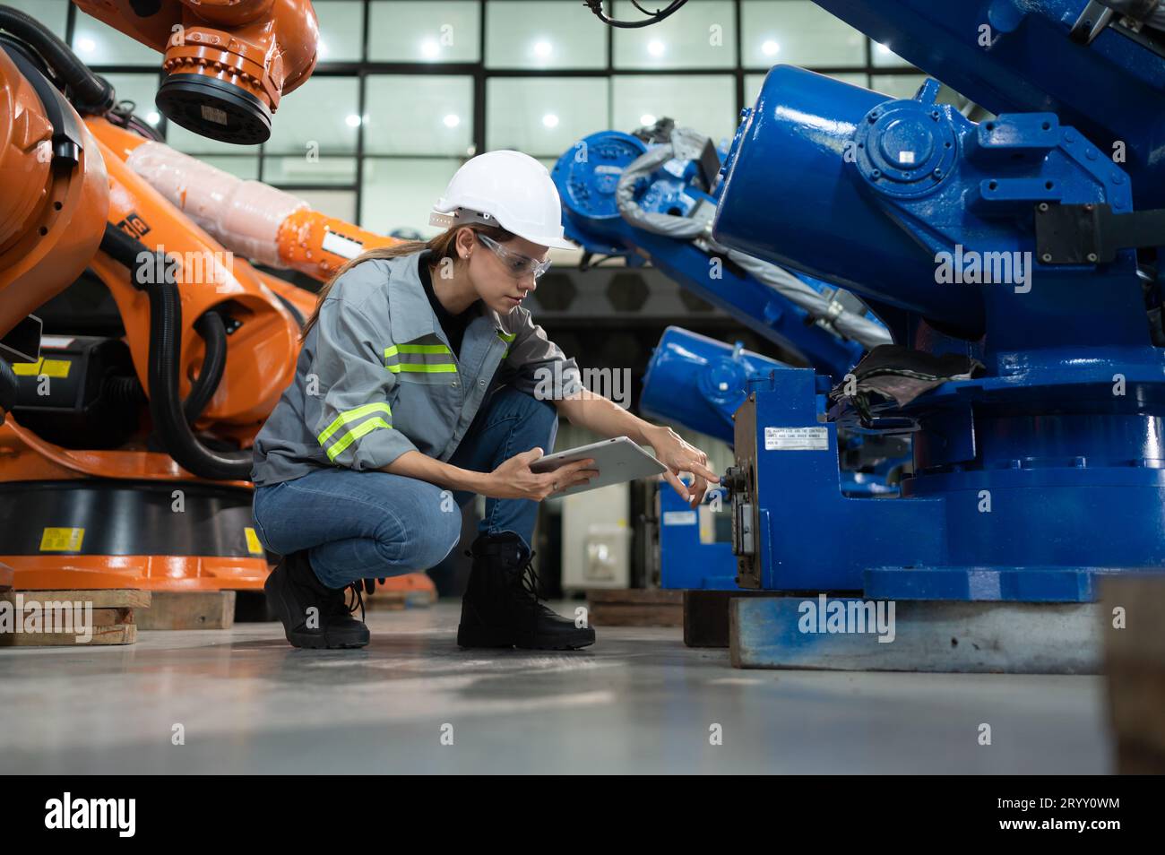 Une ingénieure installe un programme sur un bras robotique dans un entrepôt de robots. Et tester l'opération avant d'envoyer la machine t Banque D'Images
