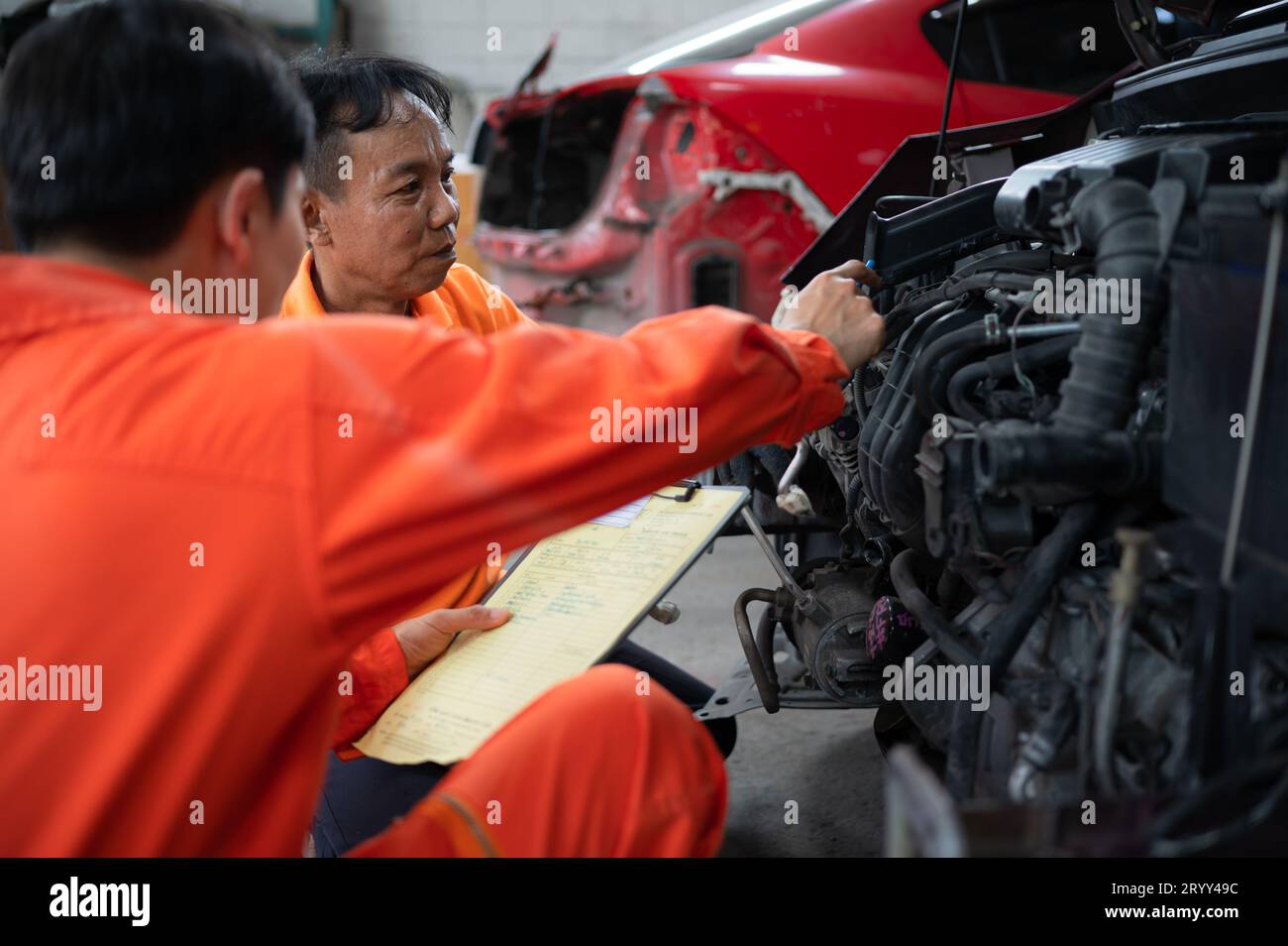 Les deux mécaniciens inspectent le moteur de la voiture d'un client qui est amené pour réparation dans un garage. Banque D'Images