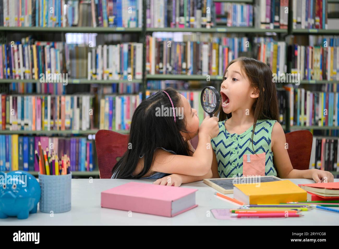 Deux petites filles mignonnes heureuses faisant le visage drôle et jouant ensemble dans la bibliothèque à l'école comme bilan de santé dentaire. Éducation et se Banque D'Images