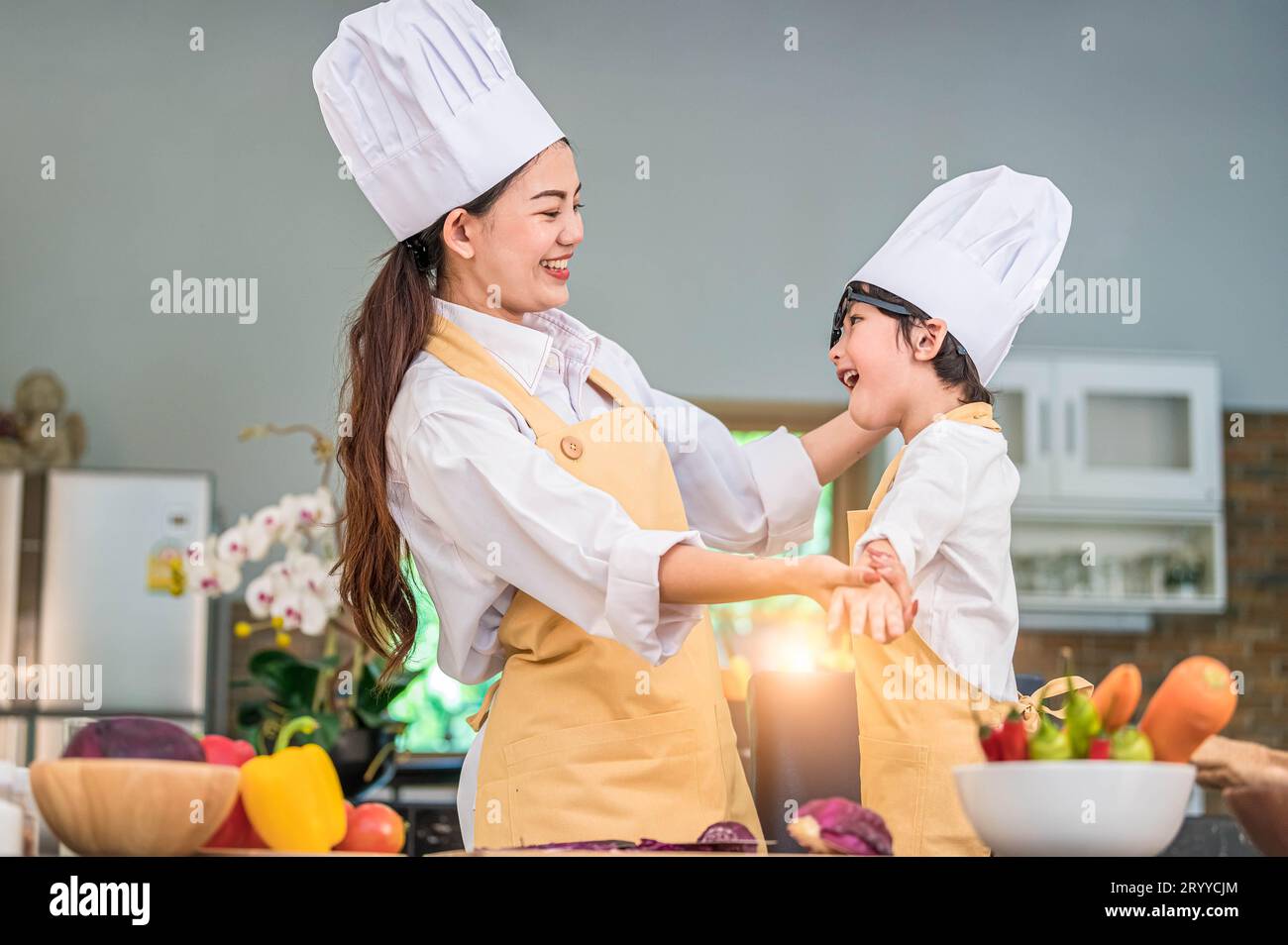 Heureuse belle femme asiatique habiller mignon petit garçon tenue de chef pour préparer à cuisiner dans la cuisine à la maison. Styles de vie des gens et F Banque D'Images