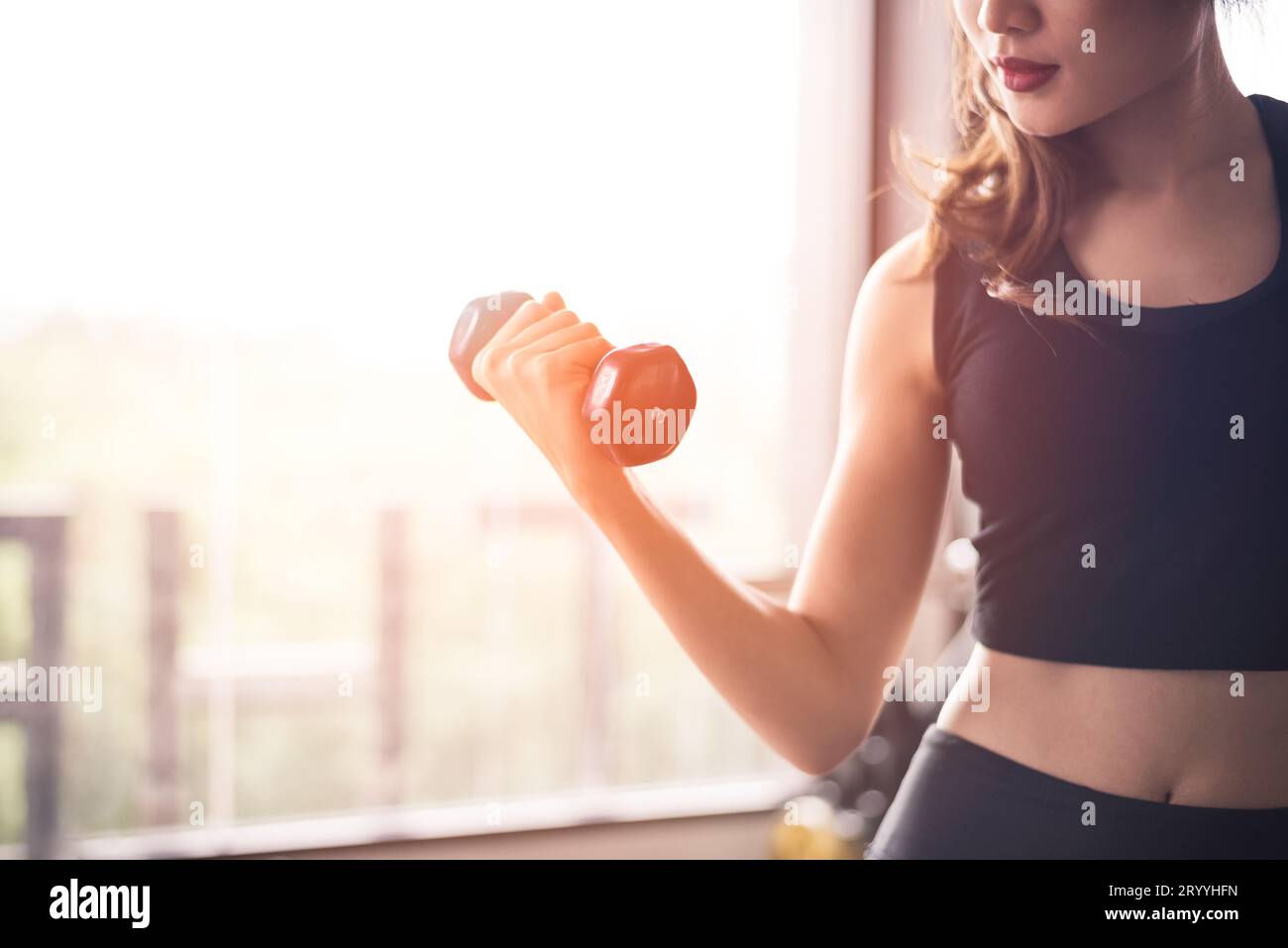 Main de femme de sport soulevant l'haltère pour la formation de poids près de la fenêtre par la main droite pour pomper le muscle de biceps. Entraînement et corps Banque D'Images