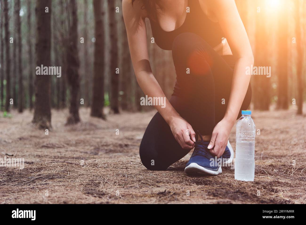 Femme attachant des lacets lors du jogging dans la forêt dos avec la bouteille d'eau potable à côté de la sienne. Nouage de corde de baskets. Personnes et lif Banque D'Images