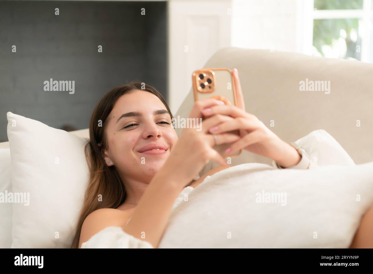 Jeune femme dans le salon de la maison le matin, accueillir des amis en ligne à l'aide d'un smartphone Banque D'Images
