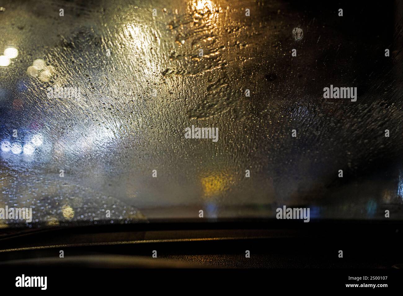 fond sur la vitre avant embuée de la voiture sous la pluie dans l'obscurité. Mauvaise visibilité sur la route et sécurité Banque D'Images