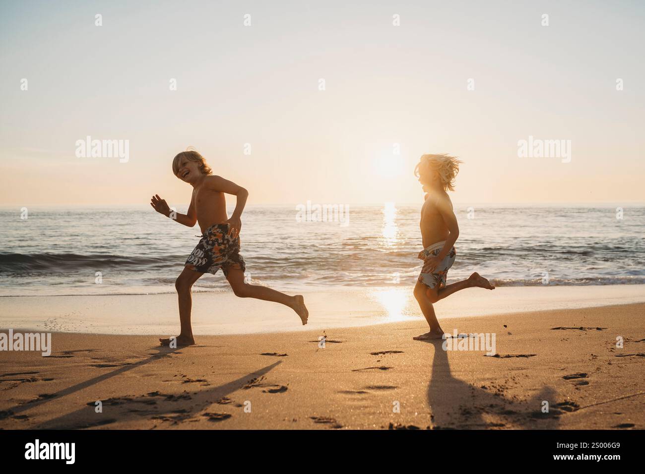 Jeunes frères s'amusant à courir à la plage pendant le coucher du soleil en Espagne Banque D'Images