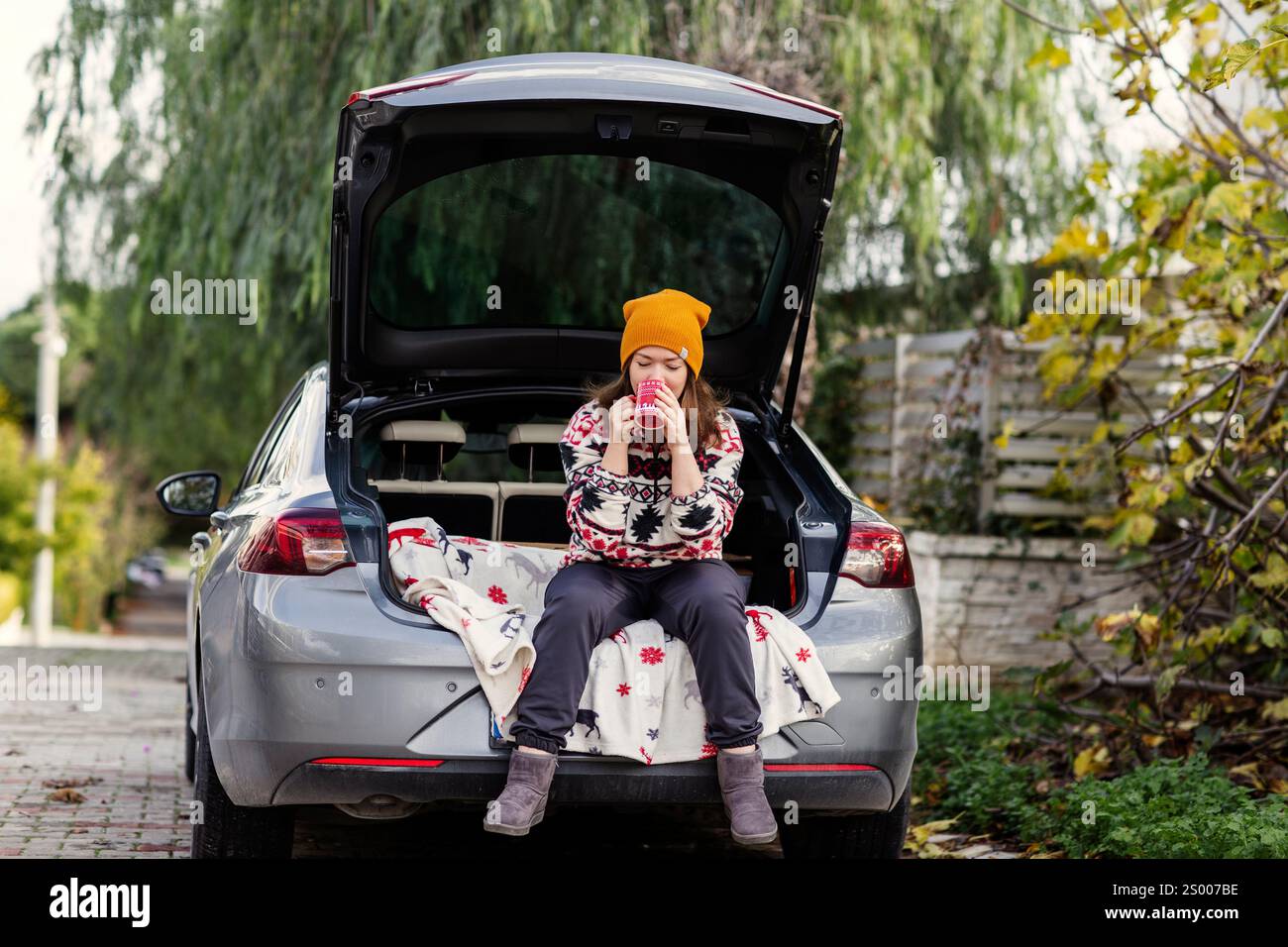 Femme en bonnet jaune assise avec du café dans le coffre de voiture Banque D'Images