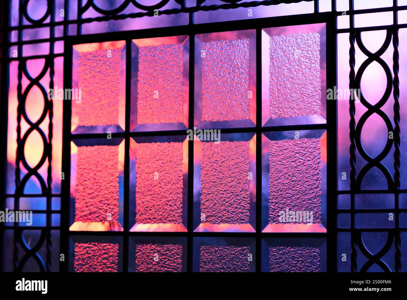 Lumière violette du soleil, coucher de soleil à travers la fenêtre de la porte en verre ornée avec ferronnerie encastrée Banque D'Images