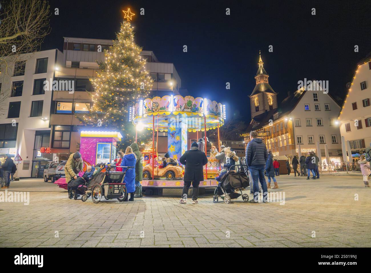 Ambiance festive sur une place avec carrousel illuminé et grand arbre de Noël, les gens appréciant la soirée, marché de Noël, Nagold, Forêt Noire, Banque D'Images