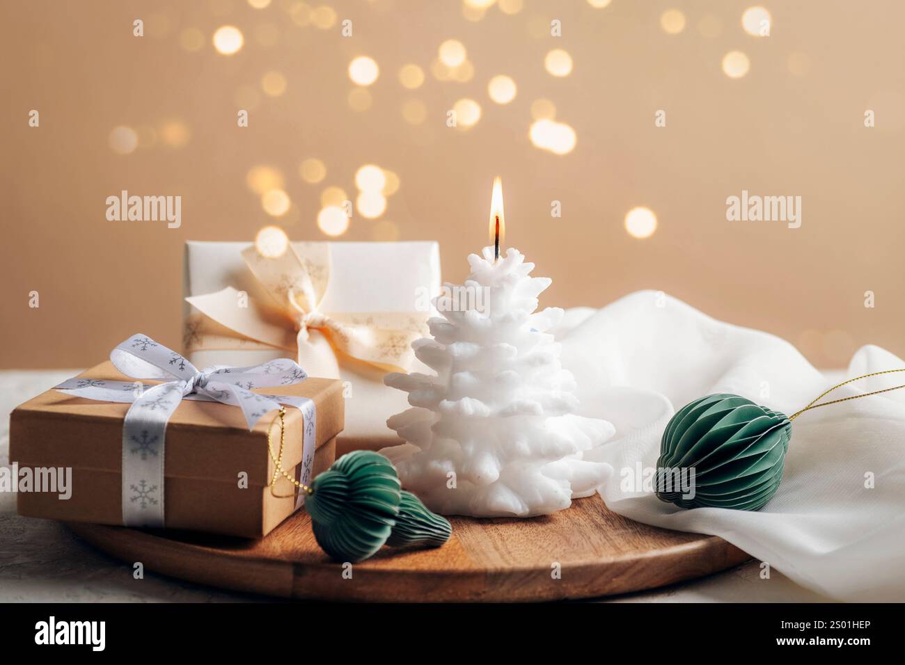 Bougie brûlante blanche festive, boîtes cadeaux et petites boules en nid d'abeille en papier sur fond beige avec lumières de Noël. Banque D'Images