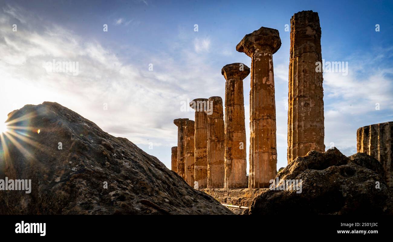 Ruines anciennes avec de hautes colonnes altérées contre un ciel spectaculaire, avec la lumière du soleil jetant un œil à travers les rochers au premier plan. Banque D'Images