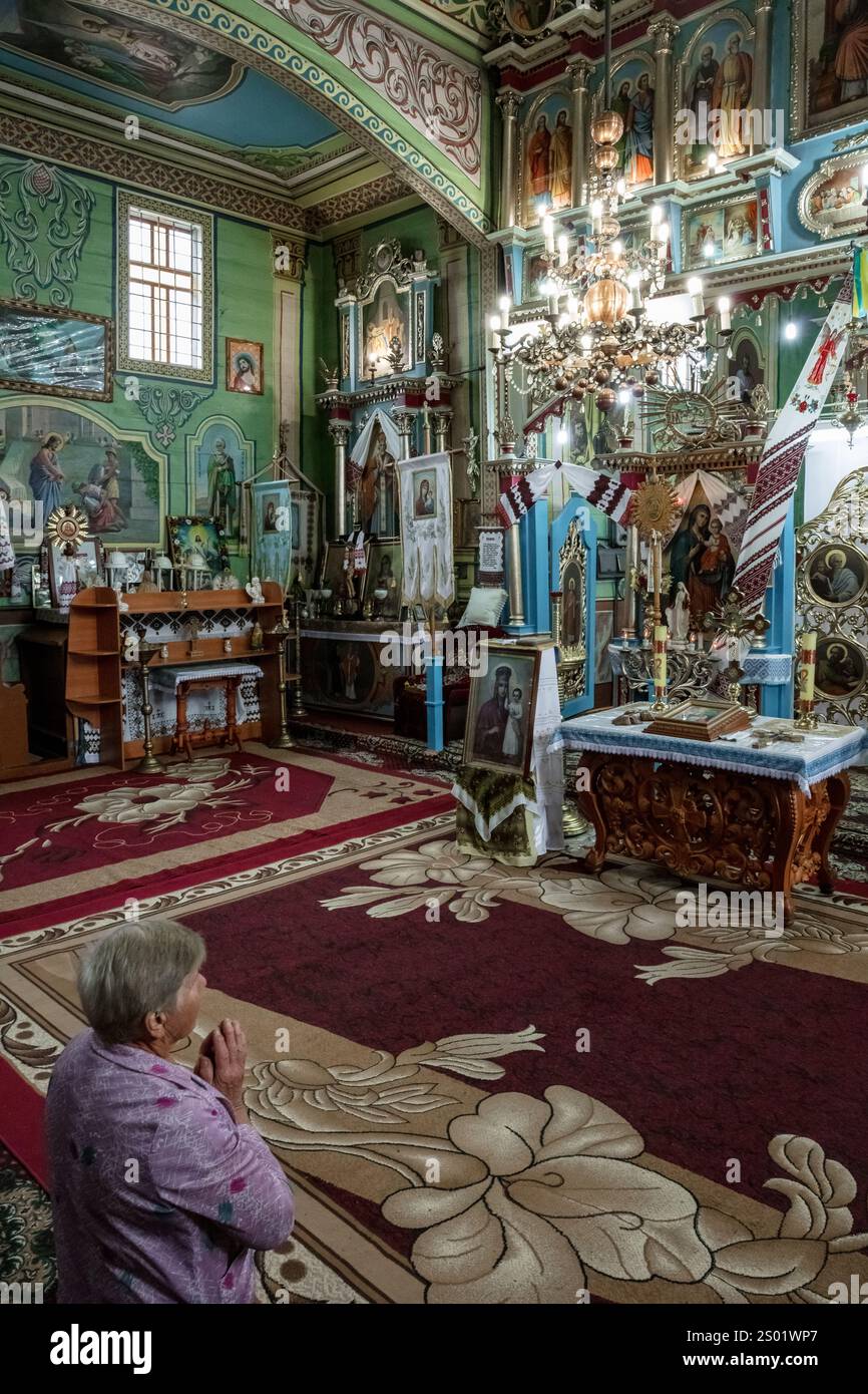 Une femme est agenouillée dans une église avec une croix sur la tête. La chambre est décorée avec des icônes religieuses et dispose d'un schéma de couleurs vertes Banque D'Images