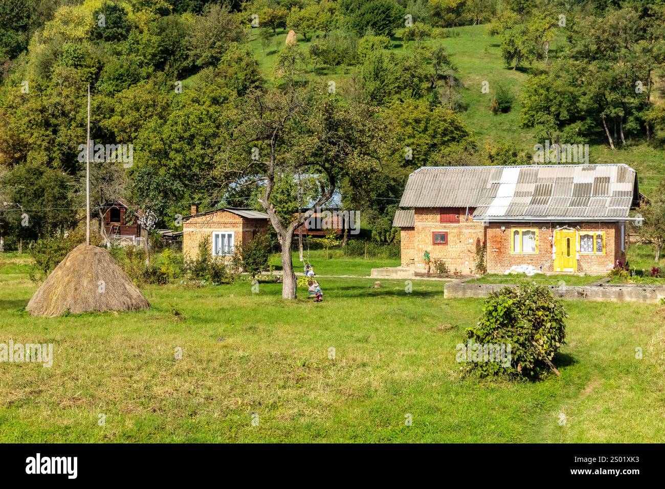 Un petit village avec quelques maisons et une grande meule de foin. Les maisons sont faites de briques et la meule de foin est au premier plan Banque D'Images