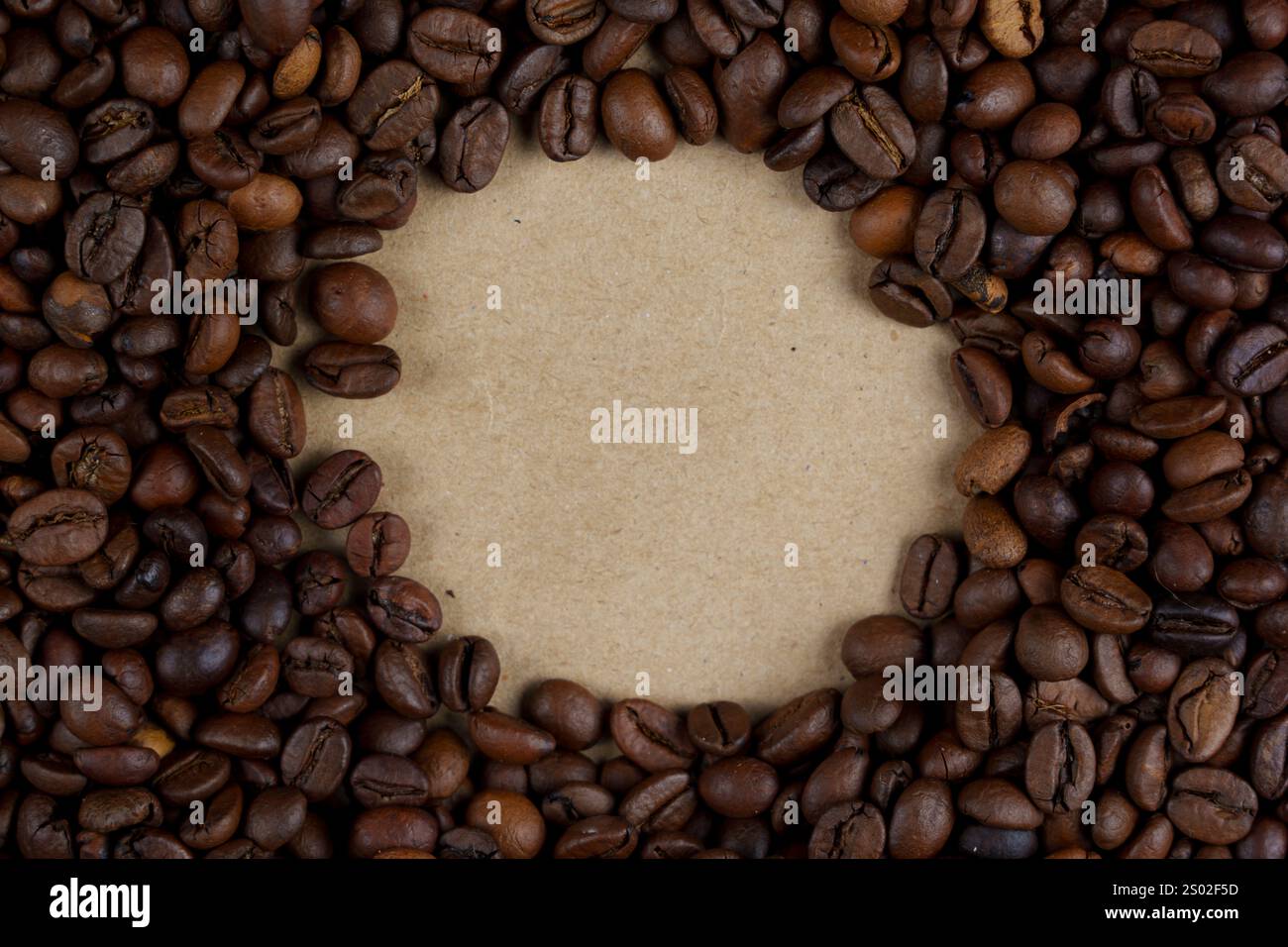 Grains de café torréfiés disposés dans un cadre circulaire autour de papier kraft vierge, idéal pour le texte ou les dessins, créant une composition naturelle et rustique, no p Banque D'Images