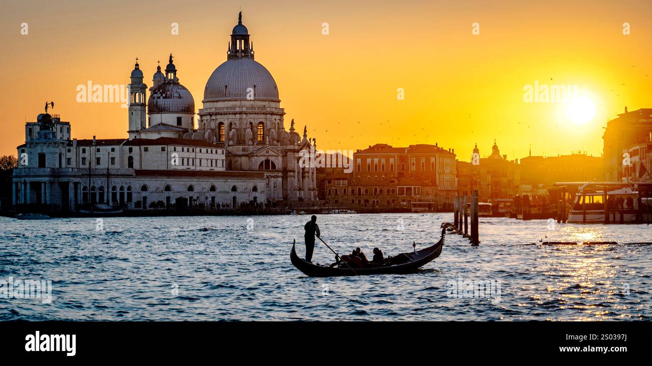 Un coucher de soleil pittoresque sur Venise, en Italie, avec une gondole sur l'eau. La silhouette d'un gondolier et des bâtiments historiques avec des dômes sont visibles Banque D'Images