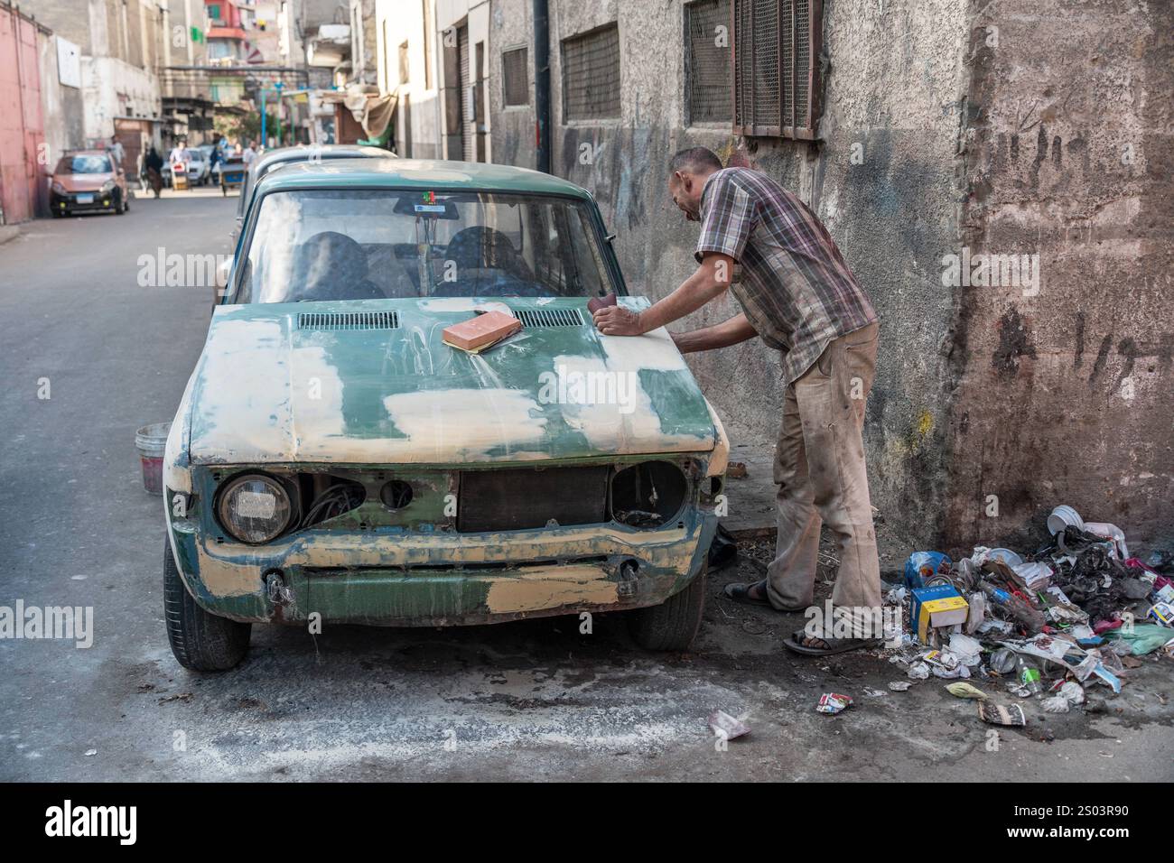 Un réparateur automobile sable une vieille voiture dans la rue d'Alexandrie, en Égypte, la préparant pour la peinture. Savoir-faire automobile urbain. Banque D'Images