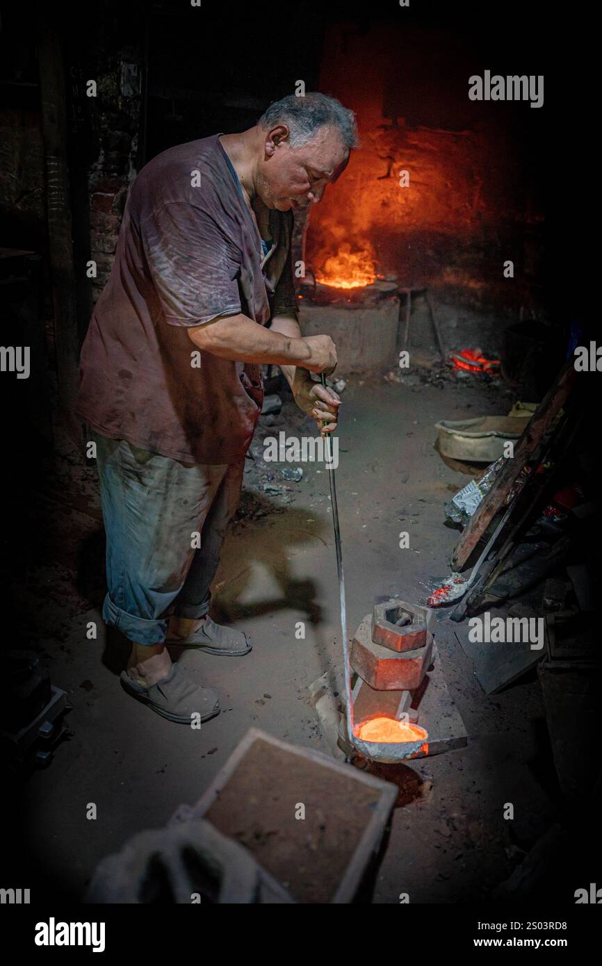 Ouvrier de fonderie dans un atelier à Alexandrie, Egypte, coulant du métal fondu dans un cadre traditionnel. Une image de fondateur en laiton reflète l'artisanat local Banque D'Images