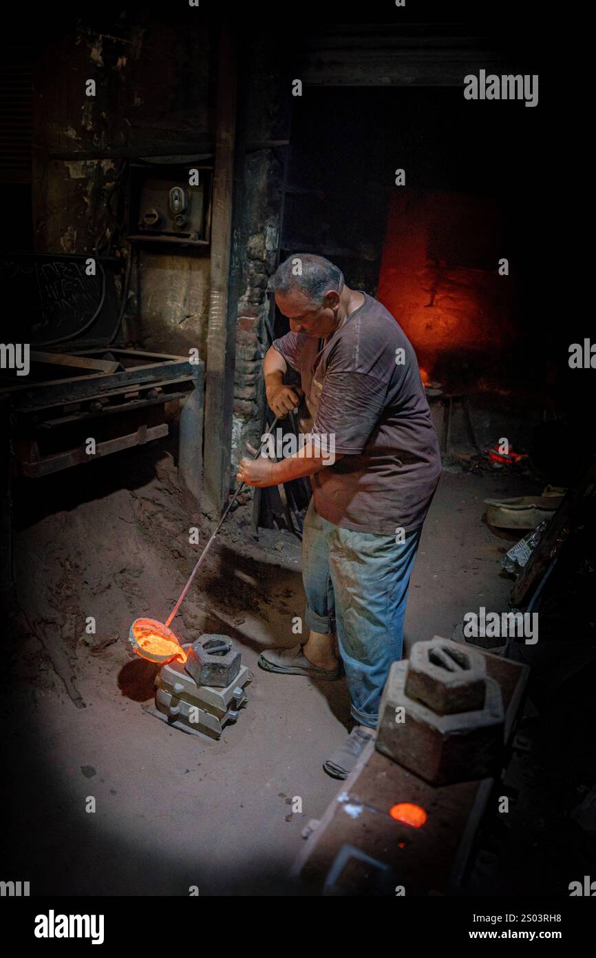 Ouvrier de fonderie dans un atelier à Alexandrie, Egypte, coulant du métal fondu dans un cadre traditionnel. Une image de fondateur en laiton reflète l'artisanat local Banque D'Images