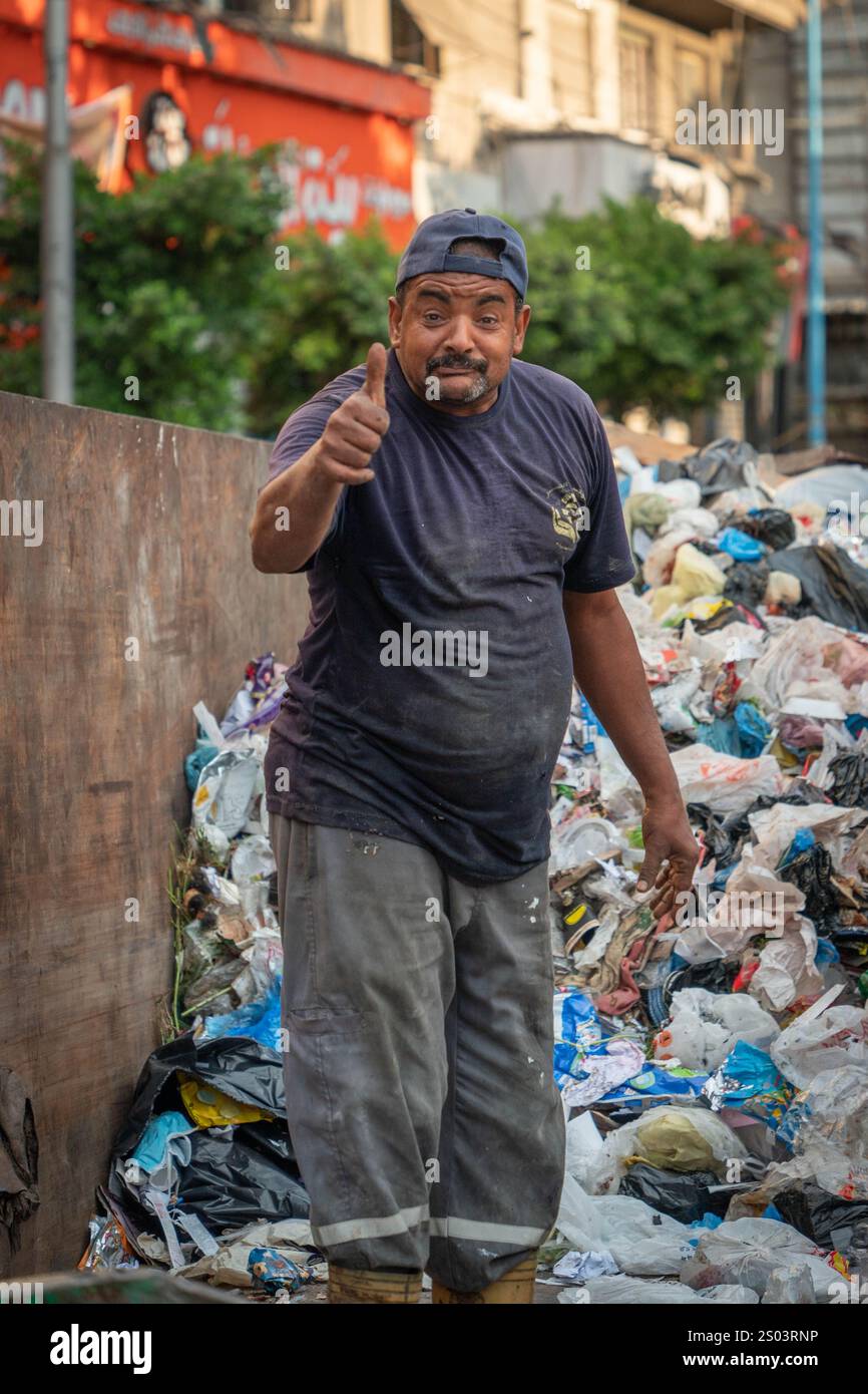Un collecteur d'ordures dédié à Alexandrie, en Égypte, donne un coup de pouce au milieu de piles de déchets, mettant en valeur la résilience et le travail acharné, la vie urbaine. Banque D'Images
