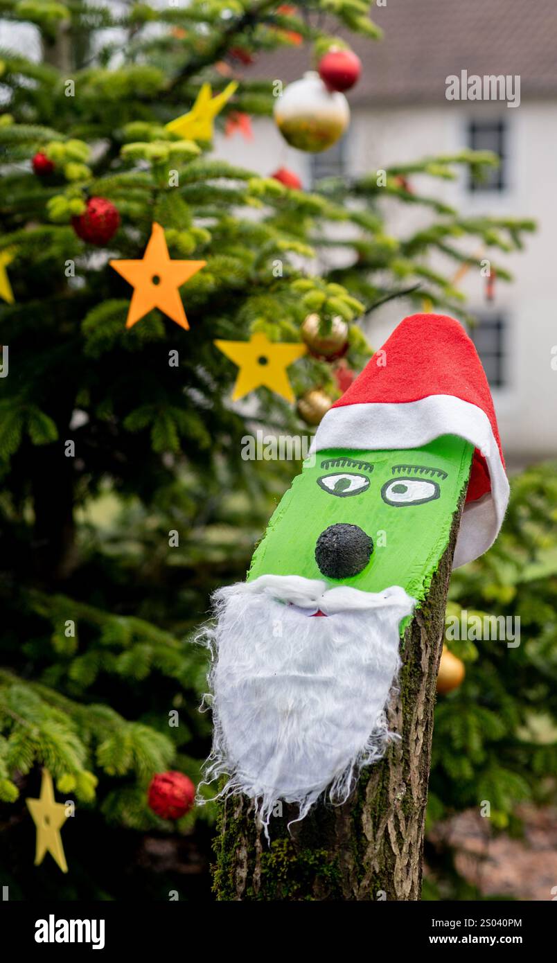 Oldenburg, Allemagne. 24 décembre 2024. Un tronc d'arbre conçu comme un personnage de film Grinch et un stand d'arbre de Noël décoré devant une école primaire. Crédit : Hauke-Christian Dittrich/dpa/Alamy Live News Banque D'Images