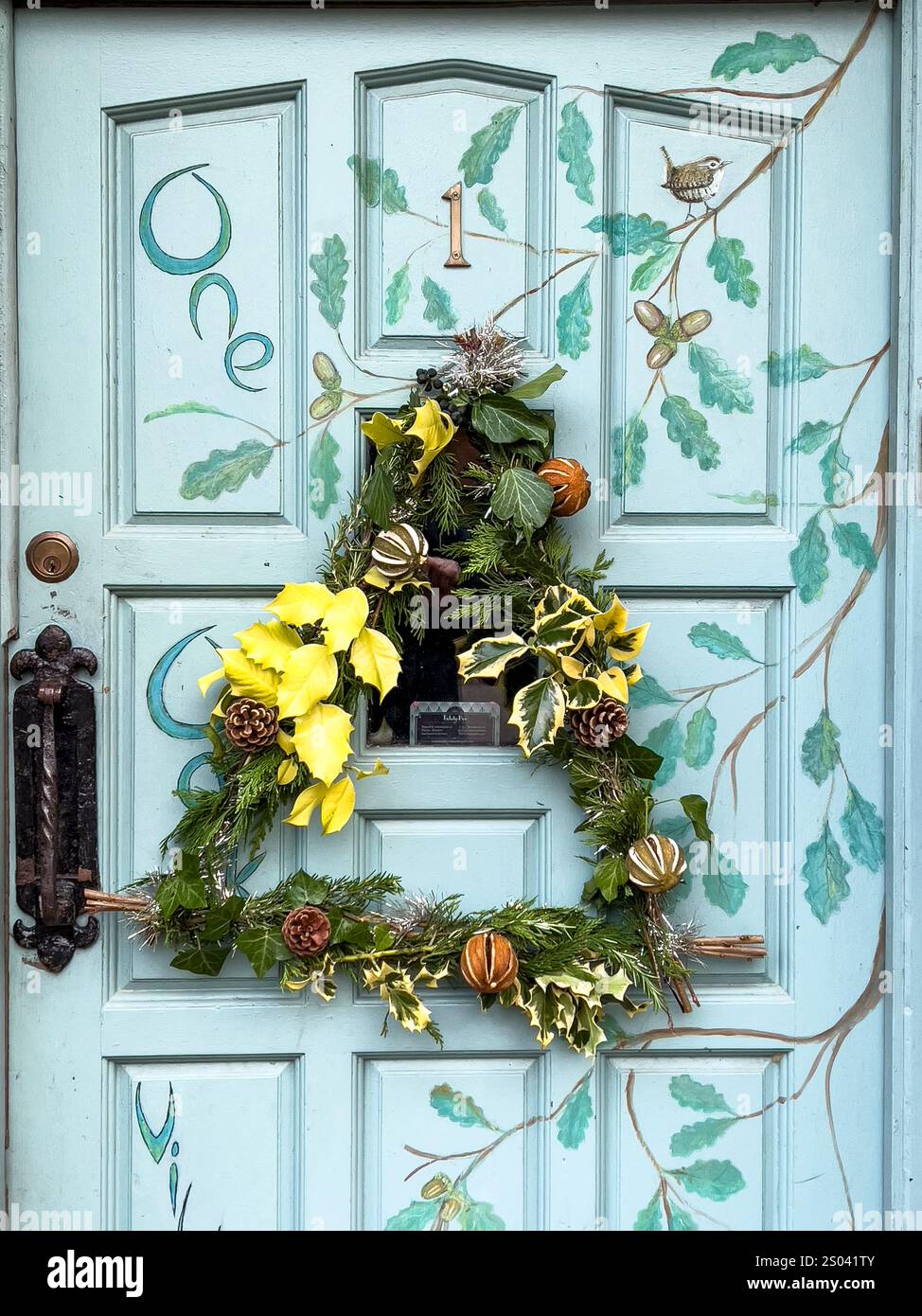 Une belle couronne de Noël saisonnière, faite maison à partir d'if, de feuilles de houx et de pommes de pin, accrochée à une porte d'entrée peinte à la main (Royaume-Uni) Banque D'Images