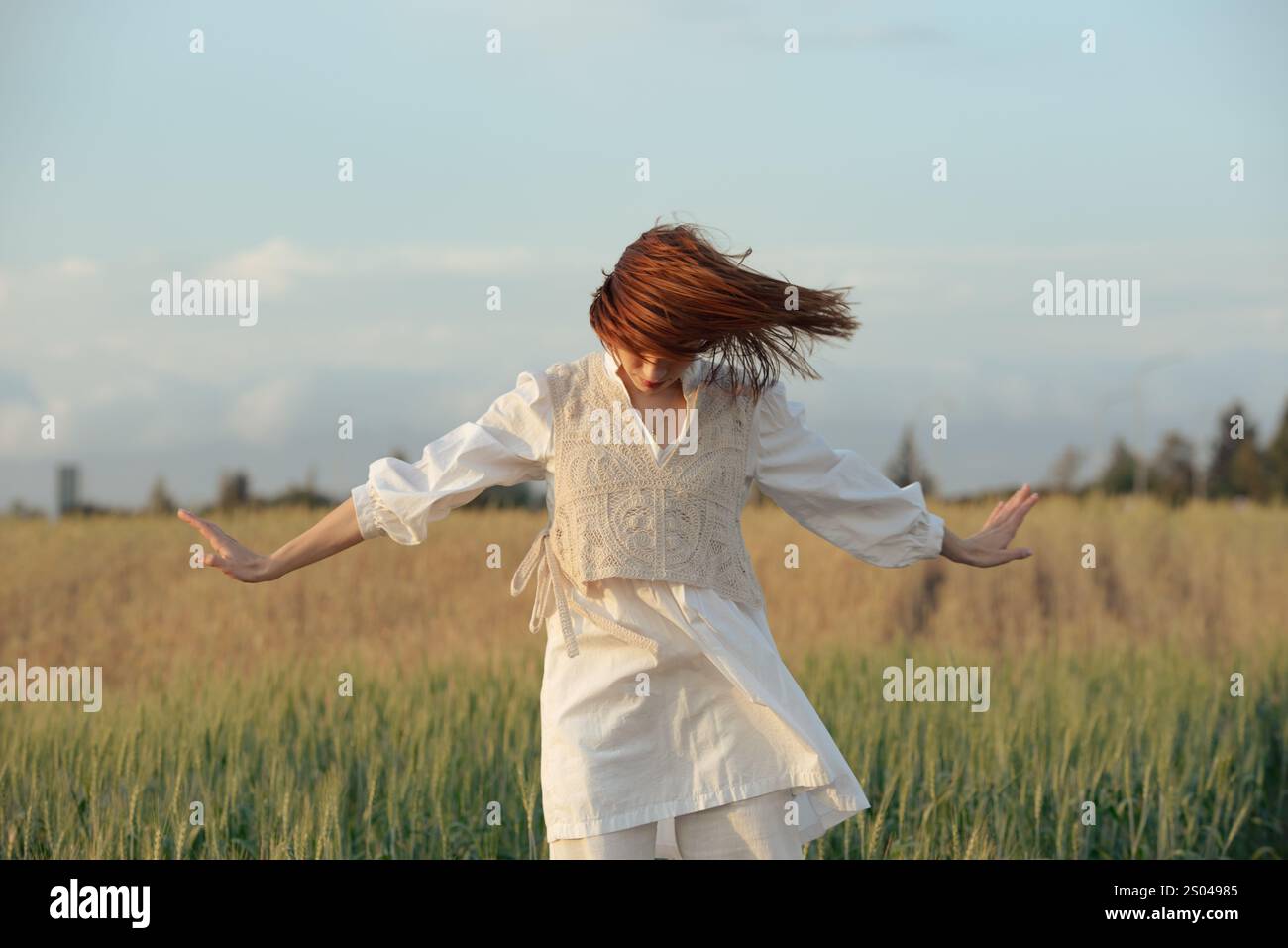 Jeune femme portant une robe blanche dansant à l'extérieur contre un ciel nuageux bleu. Femme insouciante à l'extérieur. Personnes actives dans la nature Banque D'Images