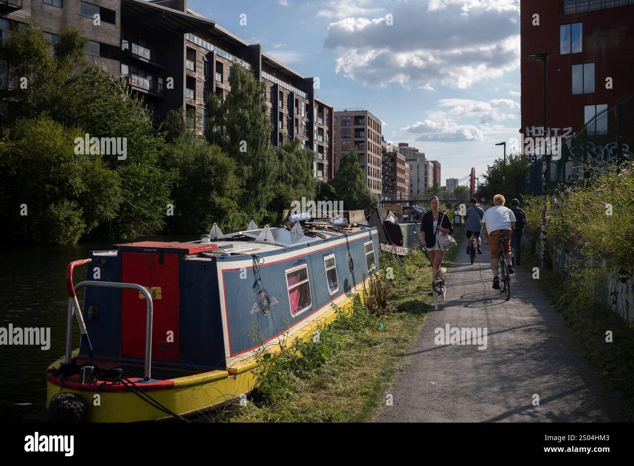 Les marcheurs passent devant une barge de canal amarrée au bord de la rivière Lee, sur la voie navigable qui traverse Hackney Wick à East London, Angleterre, Royaume-Uni Banque D'Images