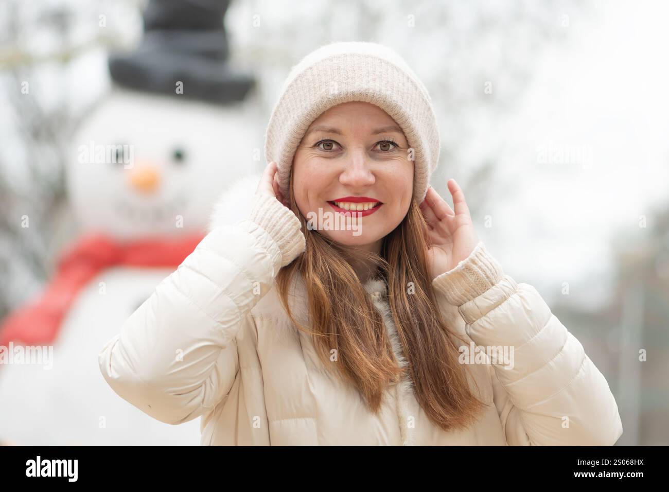 Une belle femme de 30-35 ans se tient devant un grand bonhomme de neige dans un parc enneigé en hiver Banque D'Images